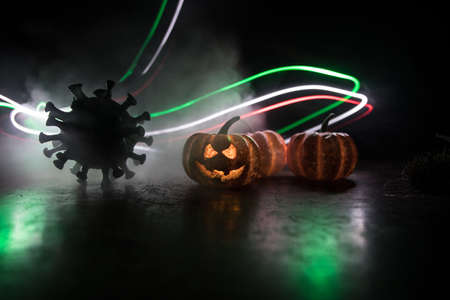 Halloween during Corona virus global pandemic concept. Glowing pumpkins and Covid novel on dark with thematic spooky decorations. Halloween pumpkin on foggy backlight. Selective focusの写真素材