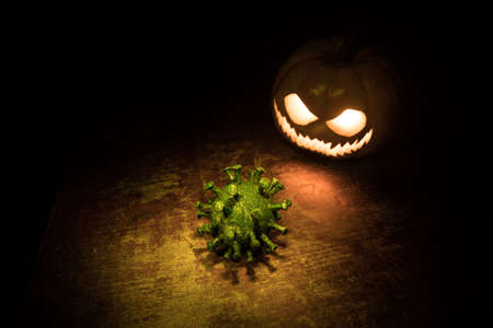 Halloween during Corona virus global pandemic concept. Glowing pumpkins and Covid novel on dark with thematic spooky decorations. Halloween pumpkin on foggy backlight. Selective focusの写真素材