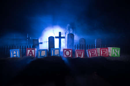 Halloween word written on wooden squares. Horror cemetery on background. Empty space, Selective focusの写真素材