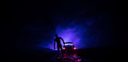 photo of a car stopped on the road lighting up a zombies. Silhouette terrible zombie night near the...