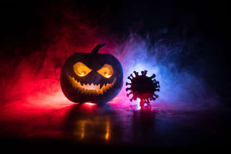 Halloween during Corona virus global pandemic concept. Glowing pumpkins and Covid novel on dark with thematic spooky decorations. Halloween pumpkin on foggy backlight. Selective focusの写真素材