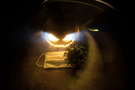 Halloween during Corona virus global pandemic concept. Glowing pumpkins and Covid novel on dark with...