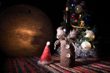 Glass of wine with Christmas decoration. Red wine in crystal glass with bottle on colorful carpet with creative New Year artwork decorations. Copy spaceの写真素材