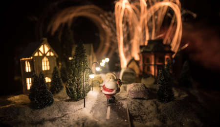 Little decorative cute small houses in snow at night in winter, Christmas and New Year miniature house in the snow at night with fir tree. Holiday concept. Selective focusの写真素材