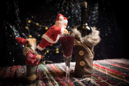 Glass of wine with Christmas decoration. Red wine in crystal glass with bottle on colorful carpet with creative New Year artwork decorations. Copy spaceの写真素材