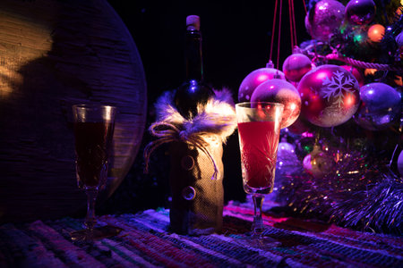 Glass of wine with Christmas decoration. Red wine in crystal glass with bottle on colorful carpet with creative New Year artwork decorations. Copy spaceの写真素材