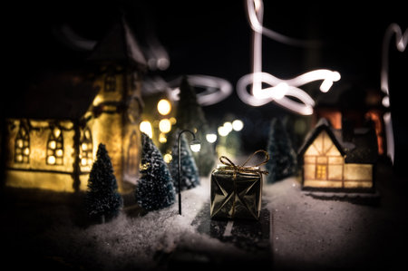 Little decorative cute small houses in snow at night in winter, Christmas and New Year miniature house in the snow at night with fir tree. Holiday concept. Selective focusの写真素材