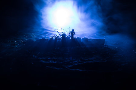 War concept. Night battle scene at sea. Dramatic toned clouds effect. Silhouette of the battle ship in night. Miniature creative table decoration. Selective focusの写真素材