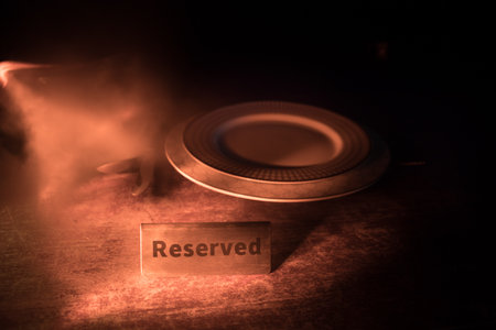 Reserved sign on the table. A tag of reservation placed on the wood table. Metal tag with reservation on dark. Reserved table in a restaurant. Creative concept with colorful lights. Selective focusの写真素材