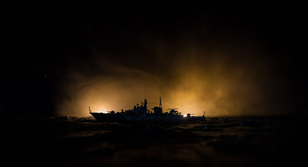 War concept. Night battle scene at sea. Dramatic toned clouds effect. Silhouette of the battle ship in night. Miniature creative table decoration. Selective focusの写真素材
