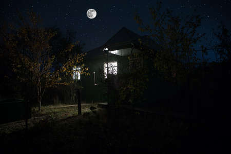 Old house with a Ghost in the forest at night or Abandoned Haunted Horror House. Old mystic building in dead tree forest. Surreal lights. Horror halloween conceptの写真素材