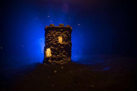 Stone defense tower at night. Medieval castle miniature with toned foggy backlight. Creative table...