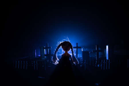 Girl walking alone in the cemetery at night. Dark toned foggy background. Horror Halloween concept. Creative artwork decorationの写真素材