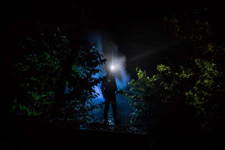 Silhouette of person standing in the dark forest with light. Horror halloween concept. strange silhouette in a dark spooky forest at nightの写真素材
