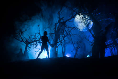 Silhouette of person standing in the dark forest. Horror halloween concept. strange silhouette in a dark spooky forest at nightの写真素材