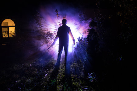 Silhouette of killer with knife standing in the dark forest with light. Horror halloween concept. strange silhouette in a dark spooky forest at nightの写真素材