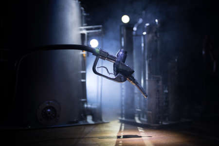 Creative concept. Silhouette of gasoline pistol miniature on dark toned foggy background. Close up. Oil pump and oil refining factory at night with fog and backlight on background. Selective focusの写真素材