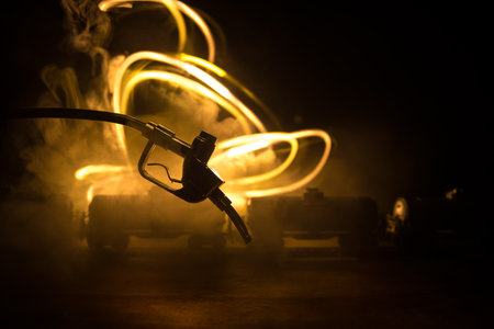 Creative concept. Silhouette of gasoline pistol miniature on dark toned foggy background. Close up. Oil pump and oil refining factory at night with fog and backlight on background. Selective focusの写真素材
