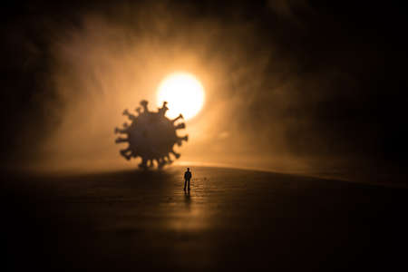virus global pandemic concept. Miniature man standing near big virus novel in dark. Creative decoration with fog and backlight. Selective focusの写真素材