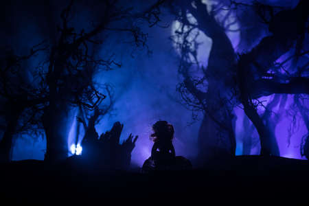 Alone girl in the dead forest at misty night. Silhouette of girl standing between trees under moonlight. Horror Halloween concept. Selective focus.の写真素材