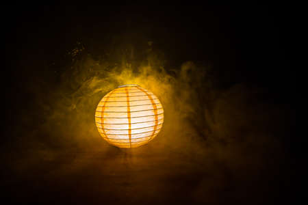 Beautiful paper lantern glowing on wooden table in dark. Selective focusの写真素材