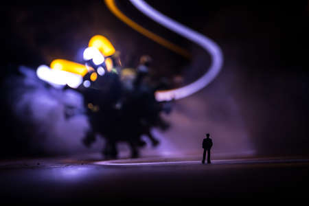 Corona virus global pandemic concept. Miniature man standing near big Corona virus novel in dark. Creative decoration with fog and backlight. Selective focusの写真素材