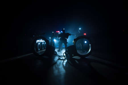 Police raid at night and you are under arrest concept. Silhouette of handcuffs with police car on backside. Image with the flashing red and blue police lights at foggy background. Selective focusの写真素材