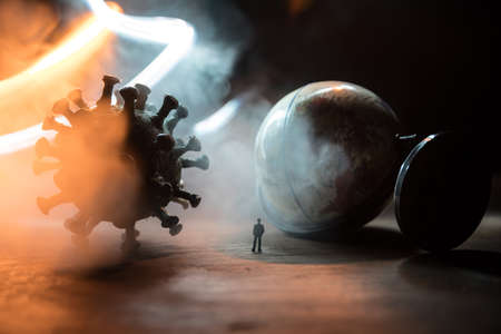 Corona virus global pandemic concept. Miniature man standing near big Corona virus novel in dark. Creative decoration with fog and backlight. Selective focusの写真素材