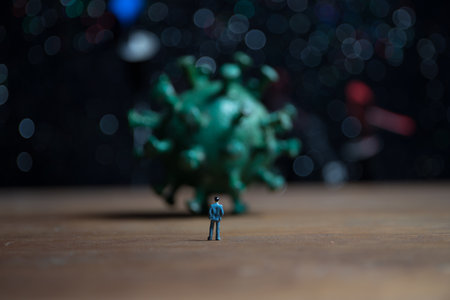 Corona virus global pandemic concept. Miniature man standing near big Corona virus novel in dark. Creative decoration with fog and backlight. Selective focusの写真素材