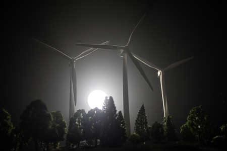 Electricity power in nature or clean energy concept. Wind Turbine producing alternative energy over the forest at night. Creative decoration with small miniature. Selective focusの写真素材