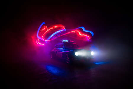Police car chasing a car at night with fog background. 911 Emergency response police car speeding to scene of crime. Creative decoration. Selective focusの写真素材