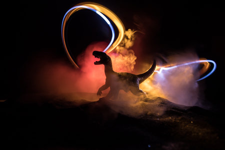 Silhouette of giant Dinosaur in foggy night. Creative decoration with little miniature. Burning misty background. Selective focusの写真素材