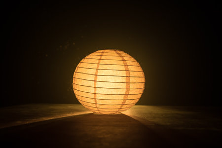 Beautiful paper lantern glowing on wooden table in dark. Selective focusの写真素材