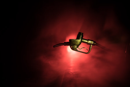 Creative concept. Silhouette of gasoline pistol miniature on dark toned foggy background. Fuel gun close up burning. Selective focusの写真素材