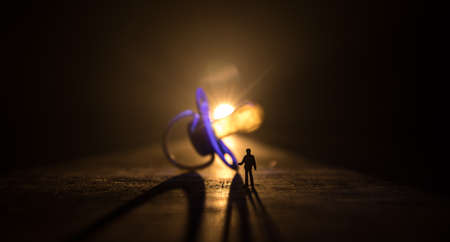 Creative concept. Man silhouette standing at giant baby pacifier on wooden table with low key toned background. Selective focusの写真素材