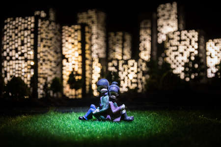 Cartoon style city buildings. Realistic city building miniatures with lights. background. Romantic couple sitting in from of nigth city in selective focusの写真素材