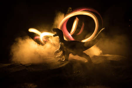 Silhouette of giant Dinosaur in foggy night. Creative decoration with little miniature. Burning misty background. Selective focusの写真素材