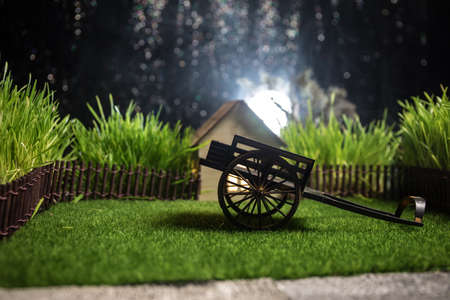 Full moon over quiet village at night. Decorative toy carriage at house with giant green grass under...