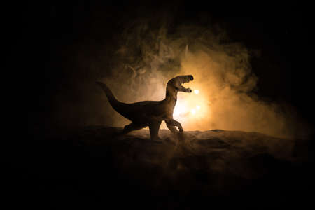Silhouette of giant Dinosaur in foggy night. Creative decoration with little miniature. Burning...
