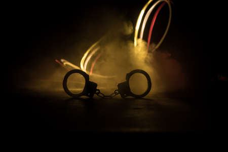 Police raid at night and you are under arrest concept. Silhouette of handcuffs with police car on backside. Image with the flashing red and blue police lights at foggy background. Selective focusの写真素材