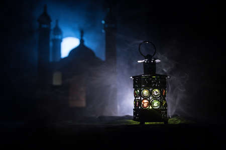 Ornamental Arabic lantern with burning candle glowing at night. Realistic mosque miniature on background. Festive greeting card, invitation for Muslim holy month Ramadan Kareem. Selective focusの写真素材
