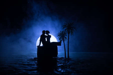 Romantic night scene. Fantasy night landscape with little island with palms and full moon over sea. Creative table decoration. Silhouette of romantic couple on uninhabited island. Selective focus.の写真素材