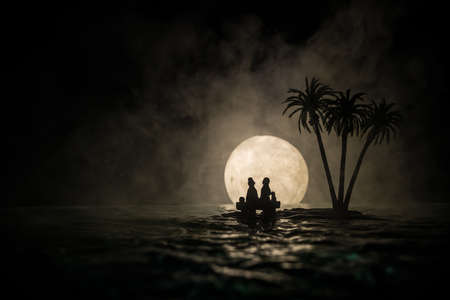 Romantic night scene. Fantasy night landscape with little island with palms and full moon over sea. Creative table decoration. Silhouette of romantic couple on uninhabited island. Selective focus.の写真素材