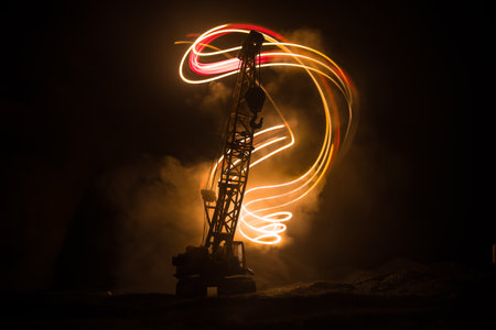 Abstract Industrial background with construction crane silhouette over amazing night sky with fog and backlight. Tower crane against the foggy sky at night. Industrial skyline. Selective focusの写真素材