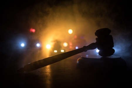 Law theme, mallet of the judge on wooden desk. Silhouette of police cars on backside. Law gavel on...
