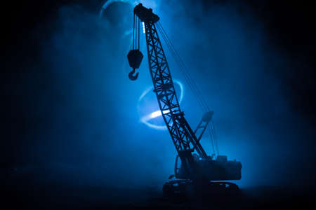 Abstract Industrial background with construction crane silhouette over amazing night sky with fog and backlight. Tower crane against the foggy sky at night. Industrial skyline. Selective focusの写真素材