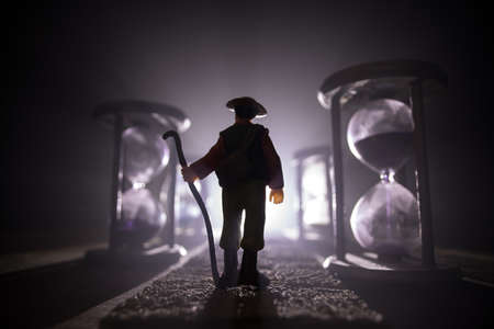 Time concept. Silhouette of a man standing between hourglasses with smoke and lights on a dark background. Surreal decorated pictureの写真素材