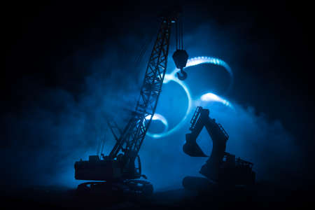 Abstract Industrial background with construction crane silhouette over amazing night sky with fog and backlight. Tower crane against the foggy sky at night. Industrial skyline. Selective focusの写真素材