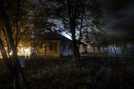 Old house with a Ghost in the forest at night or Abandoned Haunted Horror House. Old mystic building in dead tree forest. Surreal lights. Horror halloween conceptの写真素材