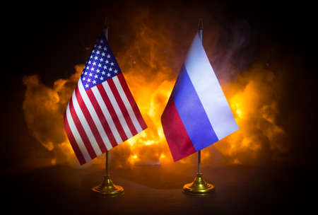 USA and Russia small flags on burning dark background. Concept of crisis of war and political...